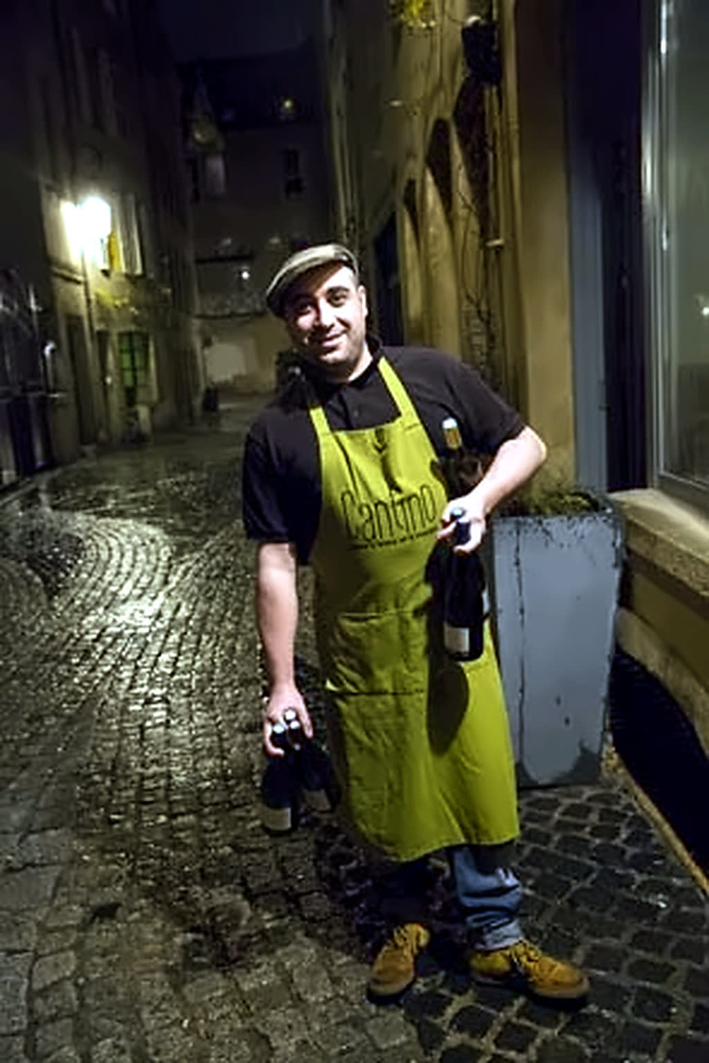 Archive 2014 : Tino en tablier Cantino, deux bouteilles à la main, dans la rue pavée